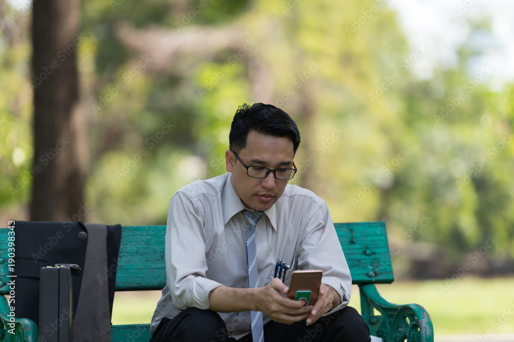 Fototapeta premium Business man sit check email on mobile phone at the Park on the way back home.