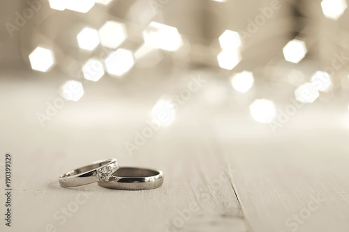Two wedding rings place on wooden floor with light bokeh background.
