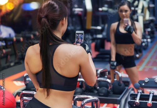 woman with smartphone taking mirror selfie in gym