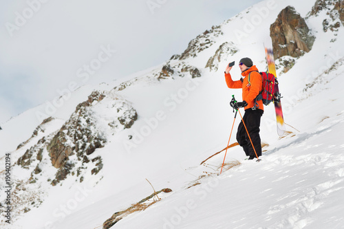 a ski freerider standing on a slope into a deep snow powder photographs the landscape on his mobile phone