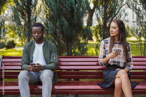 Woman sitting in park with man using smartphone © Prostock-studio