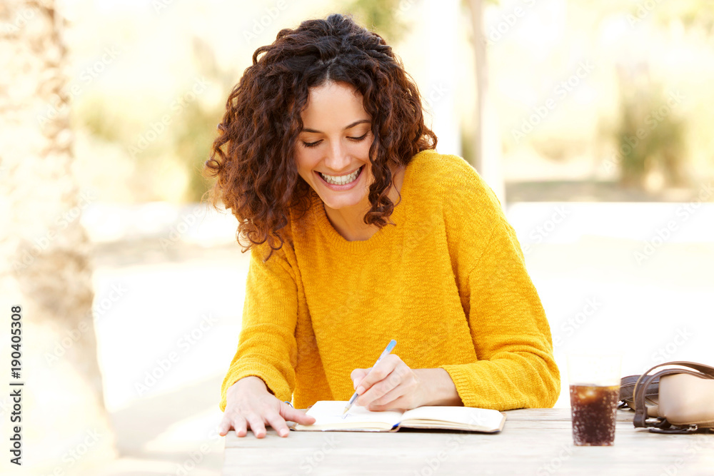 young woman sitting at table writing in diary - obrazy, fototapety, plakaty 