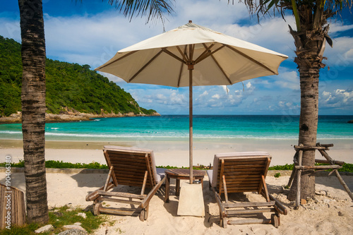 A famous tropical holiday scene with two beach chairs and an umbrella in between, flanked by palm trees, offering a beautiful view of Patok Beach on Racha Island, Phuket, Thailand. © H-AB Photography