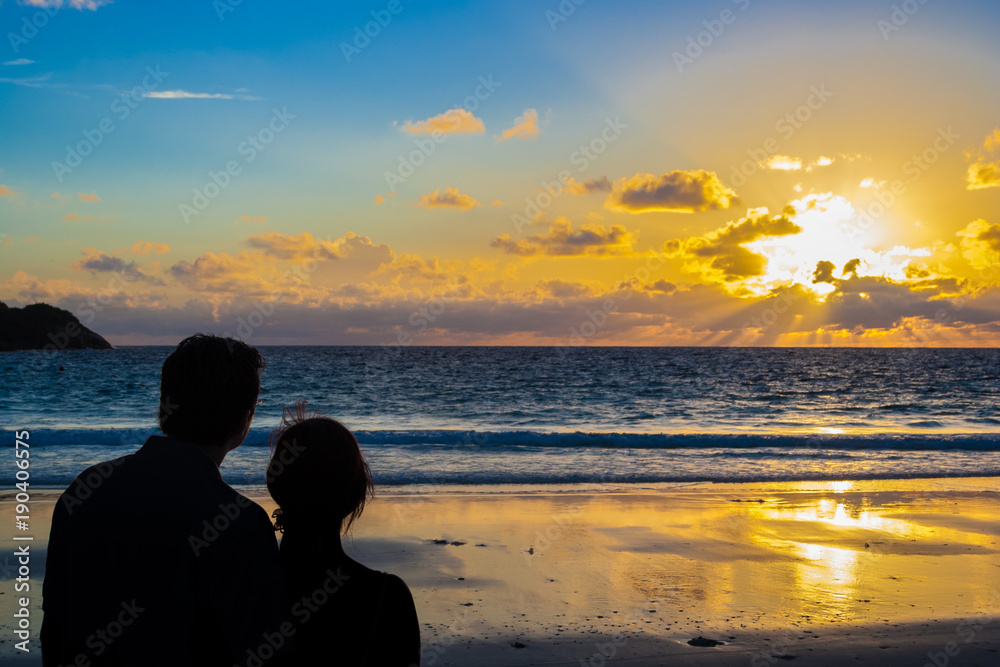 The rear view silhouette of a couple holding each other during sunset on the beach. 