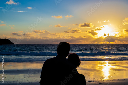 The rear view silhouette of a loving couple holding each other during sunset on the beach. 