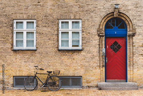 Old street, bike and red door in Copenhagen, Denmark - September, 22th, 2015. Ancient brick walls, pavement streets and bicycles are the common features of danish capital city.