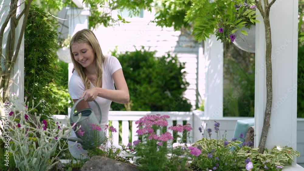 Young woman watering plants with watering can and smiling towards camera Young woman watering plants with watering can and smiling towards camera