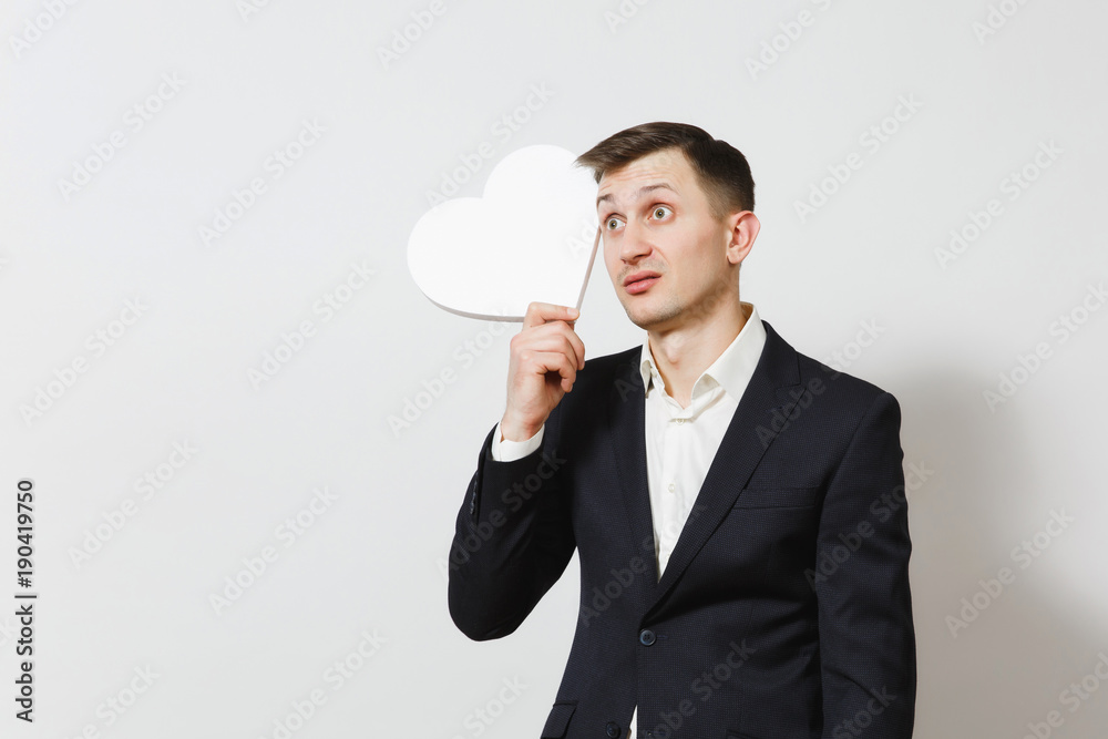 Young stunned shocked upset sad man in suit holding big white heart isolated on white background. Copy space for advertisement. St. Valentine's Day, International Women's Day, birthday holiday concept Young stunned shocked upset sad man in suit holding big white heart isolated on white background. Copy space for advertisement. St. Valentine's Day, International Women's Day, birthday holiday concept