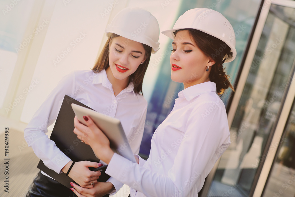 girls in business clothes and white construction helmets discuss a business plan or contract