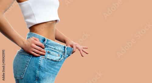 Weight loss. Woman in oversize jeans on pastel background