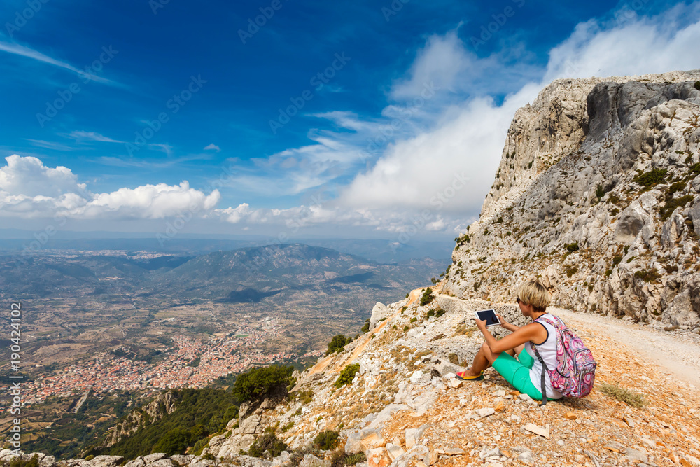 young woman tourist with the tablet on background panoramic view from the mountains on the island of Sardinia in clear weather, Monte Corrasi, Italy