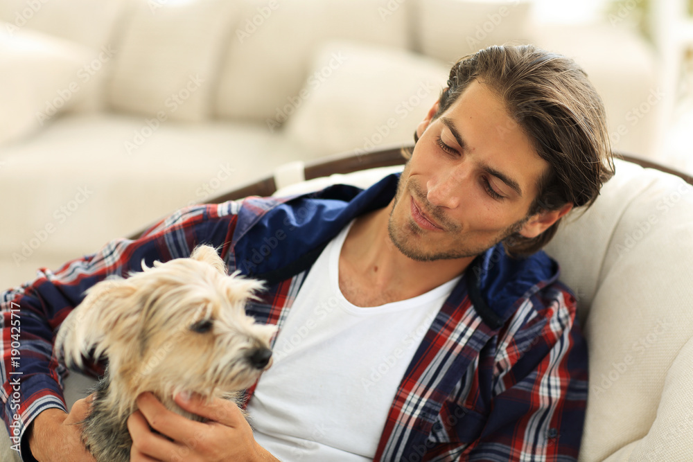 handsome guy stroking his dog while sitting in a large armchair. handsome guy stroking his dog while sitting in a large armchair.