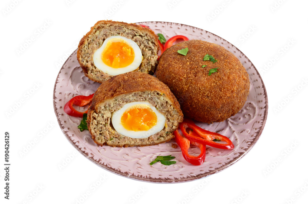 Juicy cutlet from chopped meat stuffed boiled egg on a ceramic plate isolated on a white background.