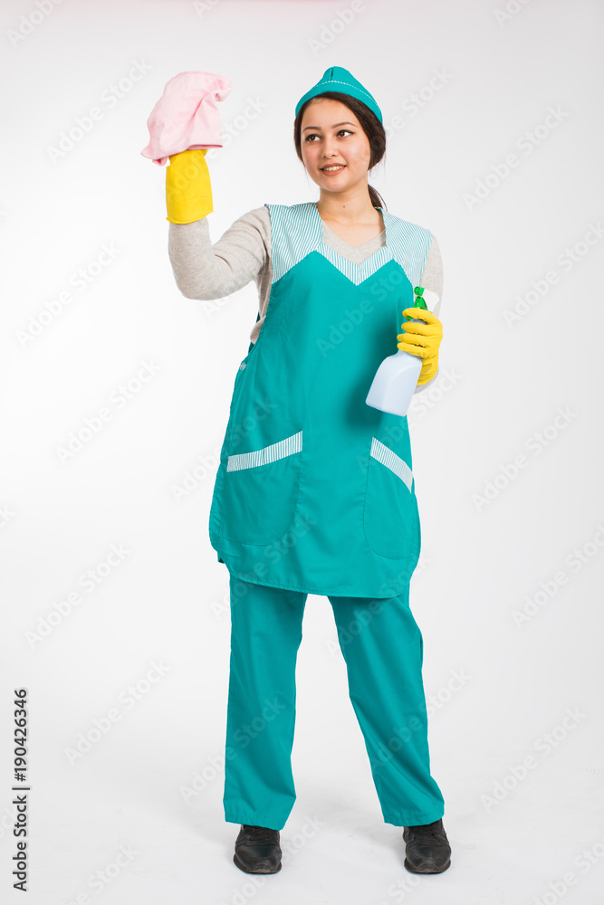 Full length photo of young brunette mais in uniform and yellow protective gloves spraying the cleaner on window, isolated on white background Full length photo of young brunette mais in uniform and yellow protective gloves spraying the cleaner on window, isolated on white background