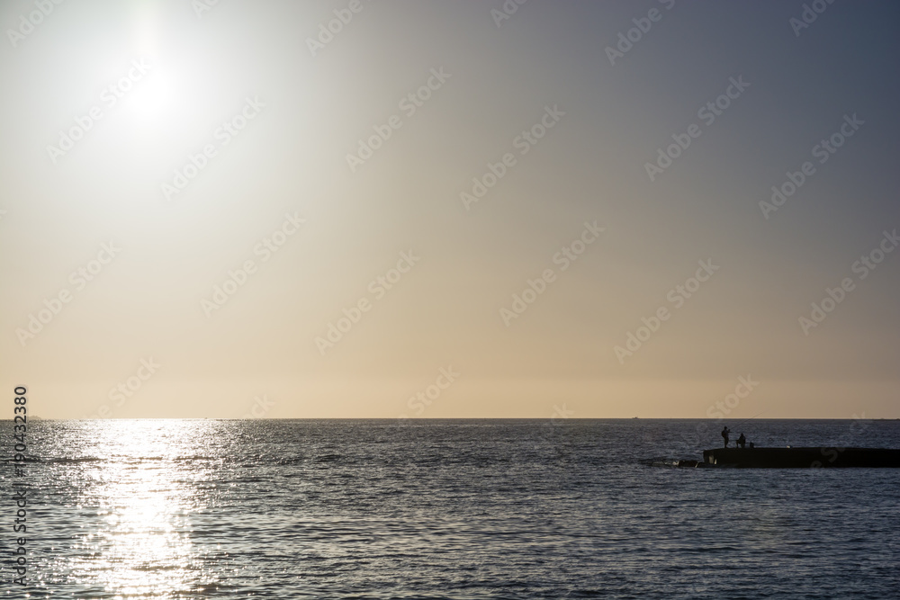 Far off of an ocean at sunset with anglers in the foreground