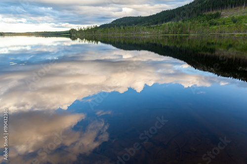 Fototapeta Naklejka Na Ścianę i Meble -  Beautiful landscape view of mountains, forest and cloudy sky reflection in calm water.