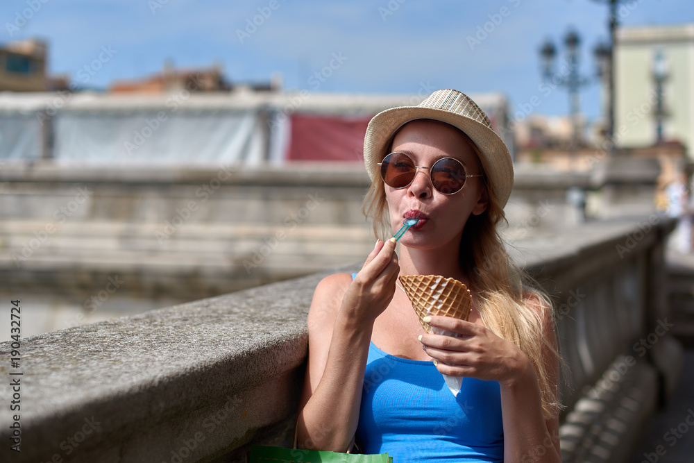 Young blondie  woman with sunglasses eating ice cream cone on a river embankment.