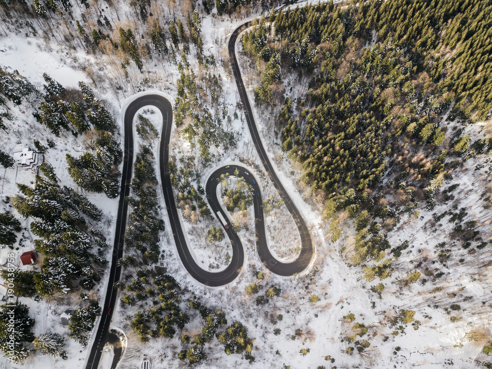 Winding road from high mountain pass, in winter time. Aerial view by drone . Romania	