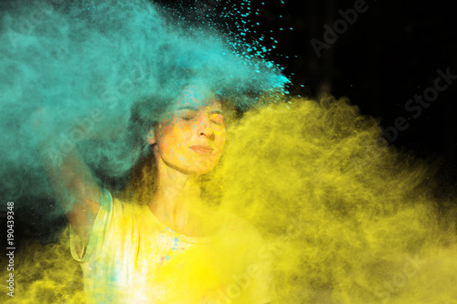 Closeup portrait of stylish young model playing with dry yellow and green paint Holi