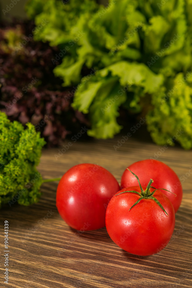 Juicy ripe tomatoes on a wooden table with fresh herbs in the background. Fresh vegetables. Juicy ripe tomatoes on a wooden table with fresh herbs in the background. Fresh vegetables.