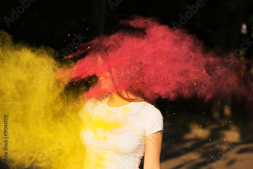 Young slim woman with exploding yellow and pink powder celebrating Holi festival