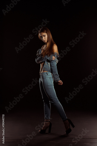 Fashionable brunette woman in trendy jeans clothes posing in the dark