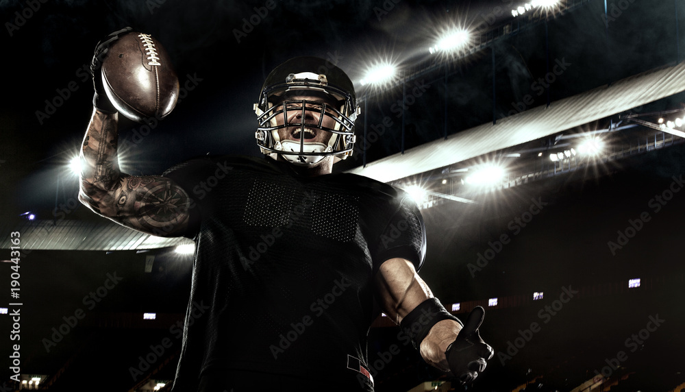 Fototapeta Sport concept. American football sportsman player holding ball on stadium.