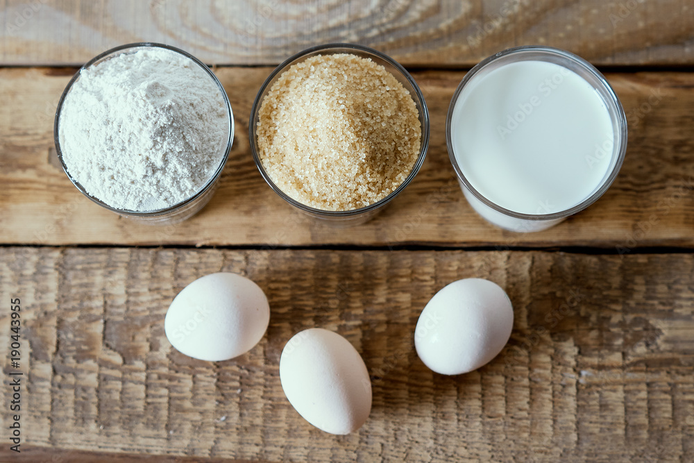 fresh milk, flour, eggs and sugar on a wooden table prepared for baking a cake fresh milk, flour, eggs and sugar on a wooden table prepared for baking a cake
