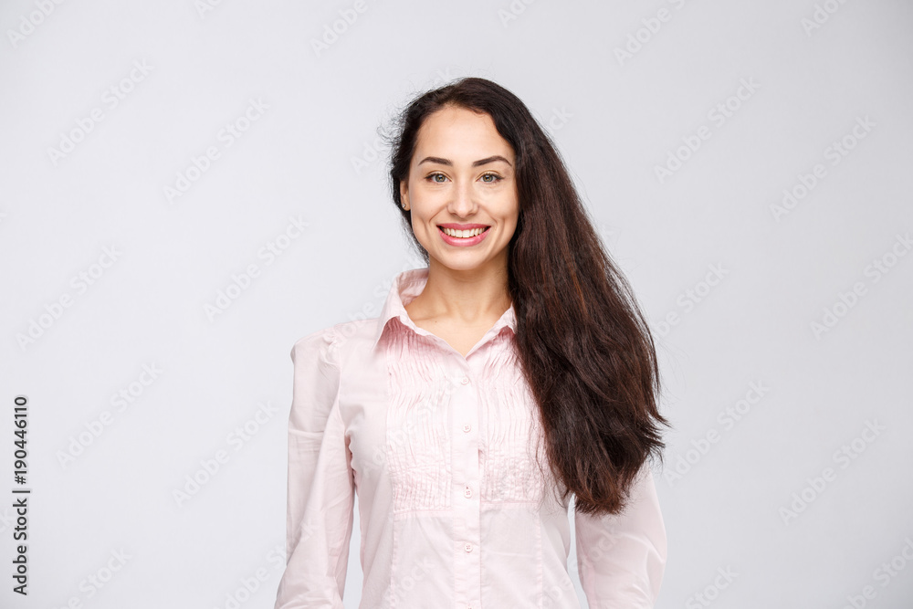 Portrait of a young woman with a charming toothy smile, black hair and brown eyes on a white background in a pink shirt. Positive and joyful emotions