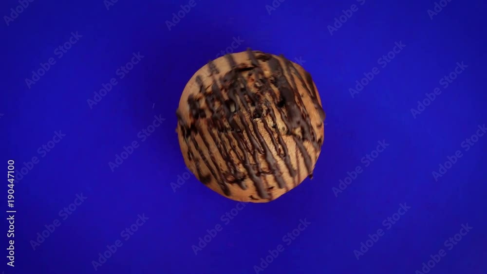 Baking, cake, fresh brown muffin rotates on a wooden background of blue color. The dessert is spinning fast. It is poured with chocolate. Great for advertising design. Baking, cake, fresh brown muffin rotates on a wooden background of blue color. The dessert is spinning fast. It is poured with chocolate. Great for advertising design.