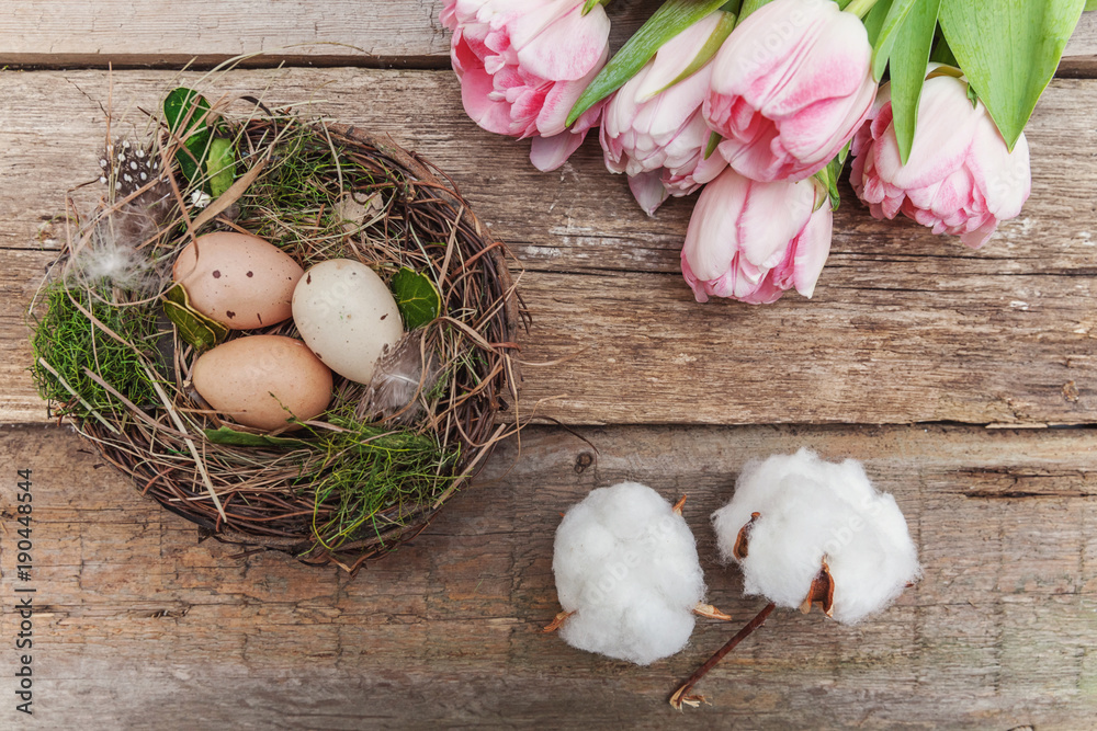 Happy easter greeting card. Easter eggs in nest with cotton, pink tulips on rustic wooden background flat lay. space for text, top view Happy easter greeting card. Easter eggs in nest with cotton, pink tulips on rustic wooden background flat lay. space for text, top view