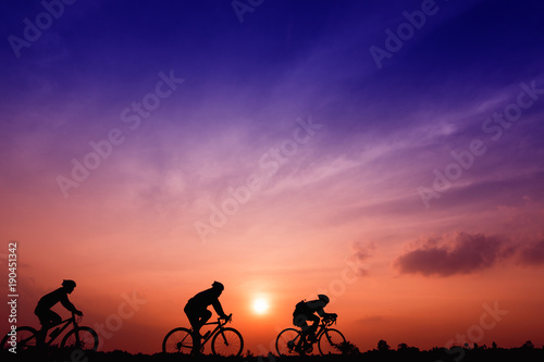 Silhouette three men ride  bikes at sunset with orange-blue sky background. Abstract Silhouette background concept.