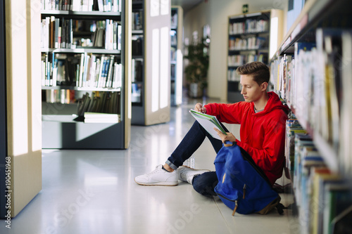 Man studying while sitting on floor at library photo