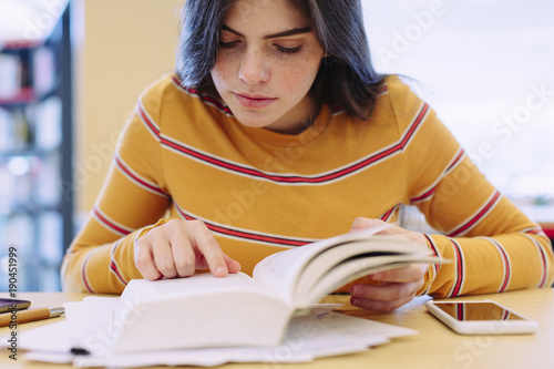 Young woman reading a book while sitting in library photo
