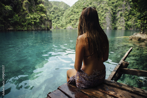 Rear view of thoughtful young woman sitting on wood over sea photo