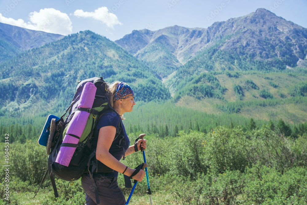 Young woman hiker with backpack and trekking poles on a sunny day on mountain trail