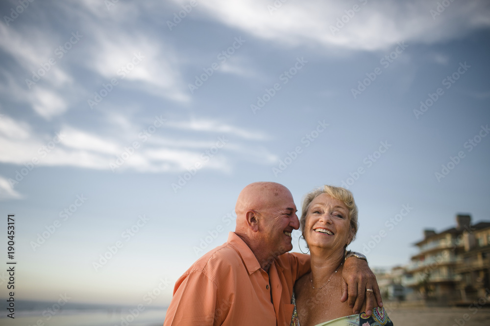 Smiling couple standing on beach against cloudy sky Smiling couple standing on beach against cloudy sky