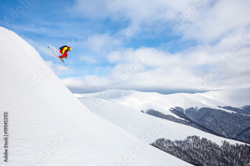 A skier is riding and jumping at mountain terrain.