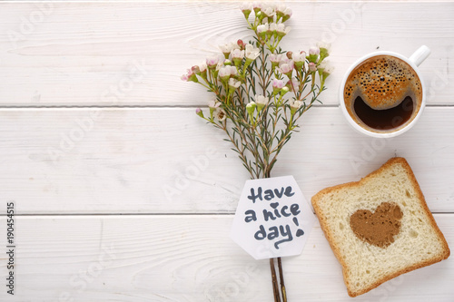 Coffee cup with flowers and toast with heart shaped cinnamon top view on white wood background