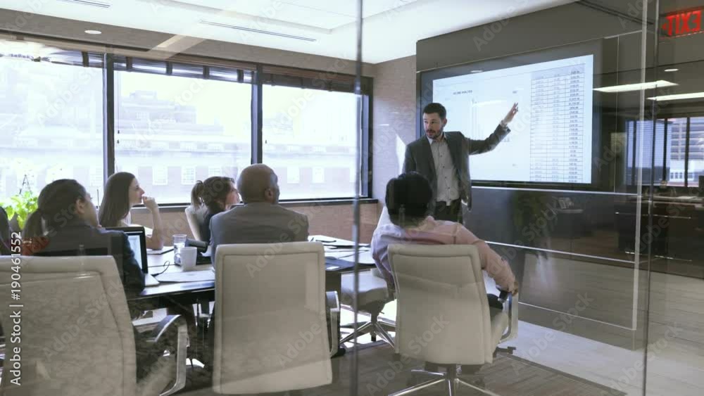 Dolly shot of business people in meeting at board room seen through glass
