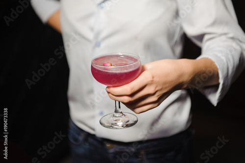 girl holds alcoholic cocktail of pink color with a rosebud