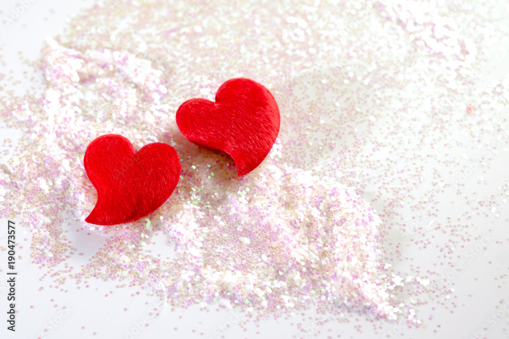 Two red hearts on white and pink glitter on white background