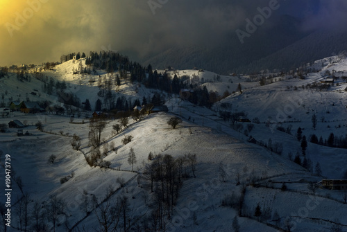Amazing winter rural lanscape with sunt hitting the clouds. Selective light of snow and of countryside houses. Morning lgolden light around clouds and smog