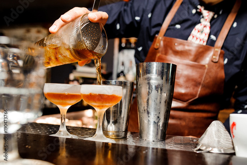 Fototapeta Naklejka Na Ścianę i Meble -  barman completes the preparation of two alcoholic cocktails using bar equipment