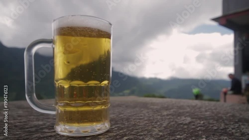 Full Beer Bubbling on Table with Mountains in Background. Close Up Slow Motion.