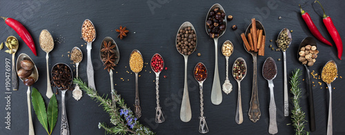 Variety of colorful spices and herbs on black stone background, top view, banner © Rawf8