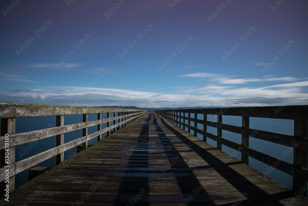 Long boardwalk pier over water on a calm blue sky day