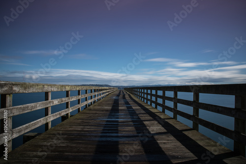 Long boardwalk pier over water on a calm blue sky day © Nicholas Steven