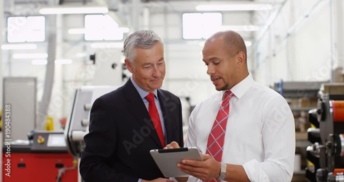 4K Business partners in factory looking at computer tablet & discussing operations. Crane shot panning downwards offering interesting change of background. Slow motion. photo