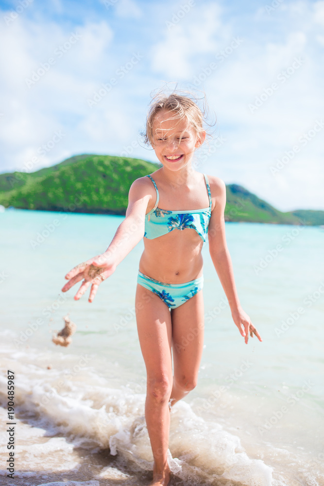 Little happy girl splashing and having fun in the shallow water. Kid in swimsuit playing with sand